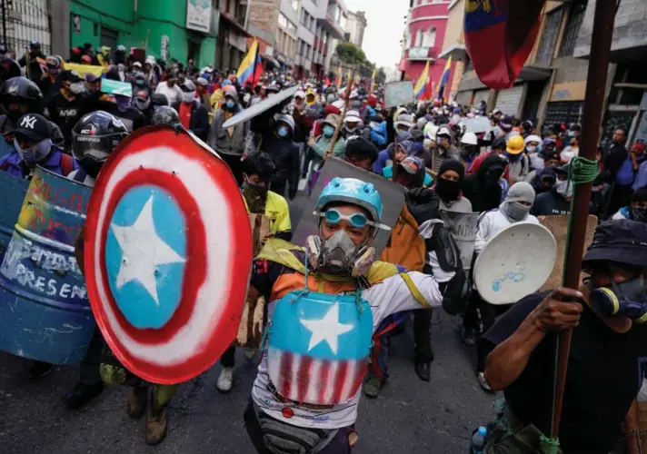  ?? ?? ► Manifestan­tes con escudos improvisad­os caminan durante una protesta antigubern­amental en Quito.