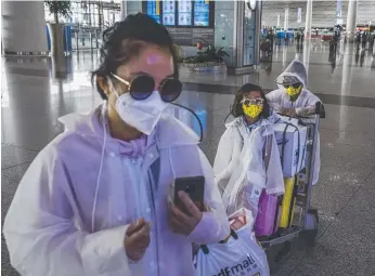  ?? Picture: KEVIN FRAYER/GETTY IMAGES ?? A Chinese family wear protective masks, sunglasses and raincoats after arriving on a flight at Beijing this week, where suppressio­n strategies have been in place.