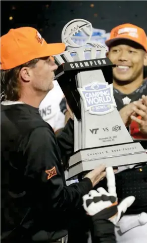  ?? (Photo by John Raoux, AP) ?? Oklahoma State coach Mike Gundy, left, holds up the trophy as linebacker Chad Whitener smiles after Oklahoma State defeated Virginia Tech 30-21 in the Camping World Bowl on Thursday.