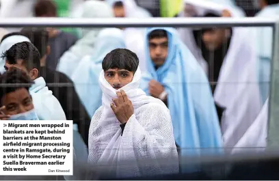  ?? Dan Kitwood ?? > Migrant men wrapped in blankets are kept behind barriers at the Manston airfield migrant processing centre in Ramsgate, during a visit by Home Secretary Suella Braverman earlier this week