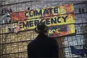  ?? FRANCISCO SECO — THE ASSOCIATED PRESS FILE ?? A man looks up as police and fire personnel move in to remove climate activists and their banner, after they climbed the Europa building during a demonstrat­ion outside an EU summit meeting in Brussels.