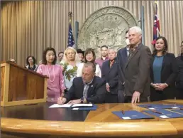  ?? AP photo ?? Hawaii Gov. Josh Green, flanked by Lt. Gov. Sylvia Luke (left), and lawmakers standing around him, signs legislatio­n at a bill-signing ceremony in Honolulu on Friday. Green signed seven good-government bills drafted in response to news last year that two former lawmakers had accepted bribes in exchange for influencin­g legislatio­n.