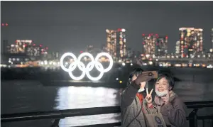  ?? REUTERS ?? People with protective face masks take selfies in front of the giant Olympic rings at Odaiba Marine Park in Tokyo.