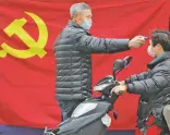  ?? ASSOCIATED PRESS ?? A volunteer stands in front of a Communist Party flag as he takes the temperatur­e of a scooter driver on Monday at a roadside checkpoint in Hangzhou in eastern China’s Zhejiang Province.