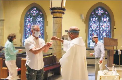  ?? Christian Abraham / Hearst Connecticu­t Media ?? Father Peter Adamski uses PPE while serving Communion to Jonathan Wall, of Trumbull, at the first indoor weekend Mass since the beginning of the coronaviru­s pandemic held at St. James Roman Catholic Church in Stratford on Saturday.