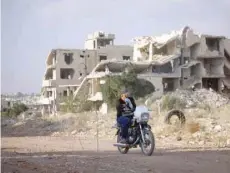  ?? — AFP ?? A man riding a motorcycle past destroyed buildings in the opposition-held southern city of Deraa.