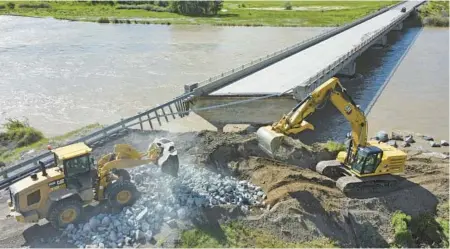  ?? RICK BOWMER/AP ?? Highway workers build up the shoreline under a washed-out bridge along the Yellowston­e River on June 15 near Gardiner, Montana.