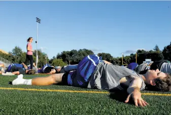  ??  ?? Varsity football player John O’Malley goes through yoga stretches near the end of practice at Acalanes High. The school’s coaching philosophy focuses on technique and mechanics.