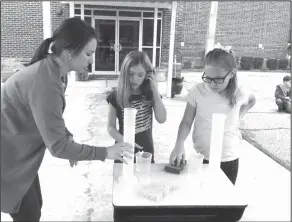  ?? Brittany Williams/News-Times ?? Water: Yocum Elementary paraprofes­sional Lyndsey Harrell checks Summer Millican and Aubree Baudoin’s water measuremen­ts during a math activity.