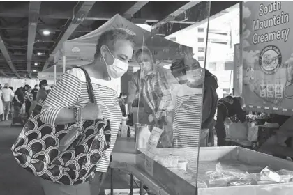  ?? AMY DAVIS/BALTIMORE SUN PHOTOS ?? Regina Smith, of Baltimore, examines cheeses offered by South Mountain Creamery of Middletown, on display behind a clear plastic shield to reduce the spread of COVID-19. The 43rd season of the Baltimore Farmers’ Market finally opened Sunday.