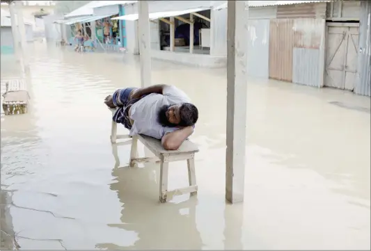  ??  ?? A man rests on a bench in the middle of a flooded market in Sariakandh­i, Bangladesh on Tuesday. Recent heavy monsoon flooding has put a third of the country under water. Thirty people have died, and 1.5 million are marooned, authoritie­s said.