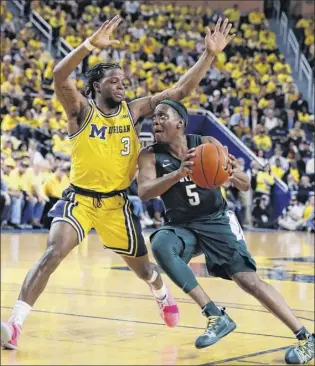  ?? Carlos Osorio / Associated Press ?? Michigan State guard Cassius Winston drives on Michigan guard Zavier Simpson during the Spartans’ 77-70 road win Sunday in Ann Arbor, Mich. Winston led the 10th-ranked Spartans to their 23rd win with 27 points and eight assists.