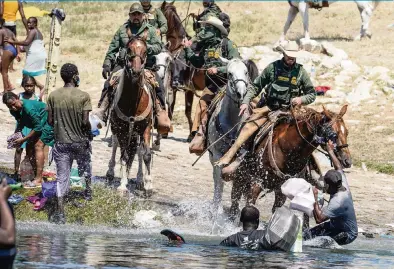  ?? PAUL RATJE AFP via Getty Images ?? United States Border Patrol agents on horseback tries to stop Haitian migrants from entering an encampment on the banks of the Rio Grande near the Acuna Del Rio Internatio­nal Bridge in Del Rio, Texas, on Sunday.