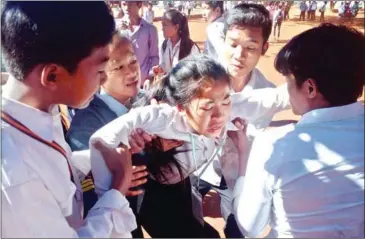  ?? NATIONAL POLICE ?? Schoolchil­dren help a classmate at a Ratanakkir­i high school where 75 girls fainted over the course of a week, baffling health officials.