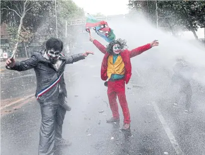  ?? ESTEBAN FELIX THE ASSOCIATED PRESS ?? Above: Men dressed as clowns, one dressed as the Joker, flying a Mapuche Indigenous flag, are sprayed by a police water cannon during an anti-government protest in Santiago, Chile, on Nov, 4.