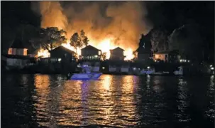  ?? Submitted photo ?? SET ABLAZE: Homeowners and good Samaritans watch from a boat as a fire rips through Four Seasons Villa Resort, 301 Kleinshore Road, late Saturday night. Passers-by noticed the glow from the flames as they were returning to their boat docks, and stopped...