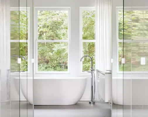  ??  ?? Les trois fenêtres au fond de la pièce et les rideaux blancs pleine hauteur procurent une belle luminosité et une sensation de légèreté à la salle de bain.