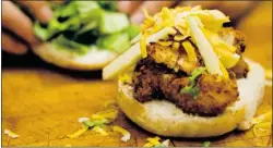  ?? Chef Tim Huska puts the finishing touches on the coco chicken burger,
a popular lunchtime dish. ??