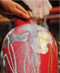  ??  ?? Yin sprays foil powder on a lacquerwar­e vase.