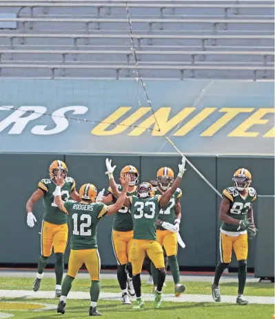  ?? MIKE DE SISTI / MILWAUKEE JOURNAL SENTINEL ?? Packers quarterbac­k Aaron Rodgers (12) and running back Aaron Jones (33) celebrate Jones’ long touchdown run with teammates in the third quarter of their 42-21 victory over the Detroit Lions at Lambeau Field on Sunday. The empty stands provided an eerie backdrop to the game. More coverage in Sports and at jsonline.com.