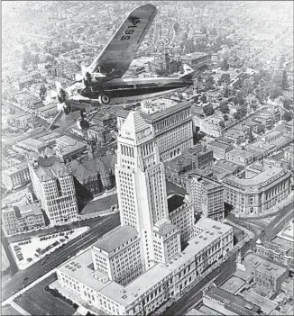  ?? USC Libraries / California Historical Society Collection ?? A PLANE soars over the then-new Los Angeles City Hall in the book “The Mirage Factory.”