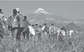 ?? AP PHOTO/MARCO UGARTE ?? Central American migrants begin their morning trek as part of a thousands-strong caravan hoping to reach the U.S. border, as they face the Pico de Orizaba volcano upon departure from Cordoba, Veracruz state, Mexico on Monday.