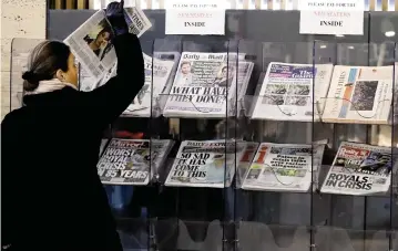  ?? FRANK AUGSTEIN AP ?? A customer in London on Tuesday takes a copy of a newspaper with a headline about the TV interview that Prince Harry and Meghan gave to Oprah Winfrey. A Buckingham Palace statement said: ‘The whole family is saddened to learn the full extent of how challengin­g the last few years have been for Harry and Meghan.’