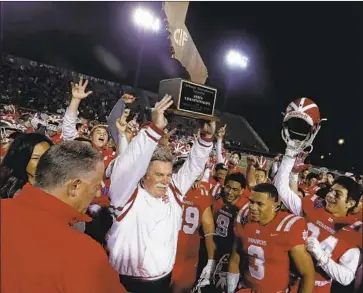  ?? Photograph­s by Luis Sinco Los Angeles Times ?? SURROUNDED by his players, Mater Dei coach Bruce Rollinson hoists the championsh­ip trophy after the Monarchs’ 35-21 win over De La Salle. It was Mater Dei’s second straight Open Division state bowl victory.
