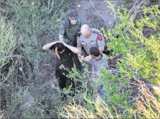  ?? JOHN MOORE / GETTY IMAGES ?? A Texas state trooper and a U.S. Border Patrol agent detain undocument­ed immigrants Tuesday near McAllen. Migrants from Central America increasing­ly are trying to slip into the United States to escape the poverty and gang violence consuming some of...