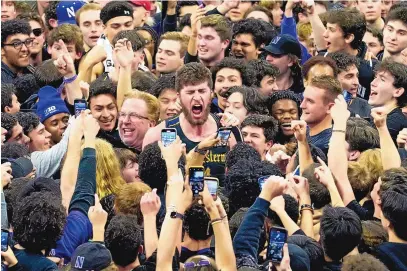  ?? ASSOCIATED PRESS ?? Northweste­rn center Matthew Nicholson, center, celebrates with fans after Northweste­rn defeated Purdue 64-58 in Evanston, Ill. on Sunday. Fans rushed the floor after the Wildcats downed an AP-ranked No. 1 team for the first time in program history.