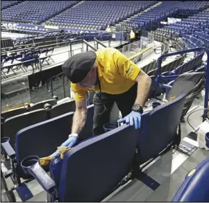  ?? Associated Press ?? CANCELED — Luis Rivera, left, sanitizes seats in Bridgeston­e Arena after the remaining NCAA college basketball games in the Southeaste­rn Conference tournament were canceled due to Coronaviru­s concerns on March 12, 2020, in Nashville, Tenn. Sports, as we knew them, ended that day. Now, there are several protocols put in place that might last for years to come.