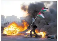  ?? AP/NASSER NASSER ?? A demonstrat­or carries a Palestinia­n flag Saturday during clashes with Israeli troops in the West Bank city of Ramallah, one of several “day of rage” protests in the West Bank and Gaza.