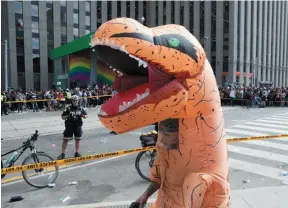  ?? CP PHOTO ?? A man in an inflatable Raptor costume walks by as police stand in a cordoned off area of Queen and Bay streets in Toronto on Monday, after two people were shot and injured during the Toronto Raptors victory parade.