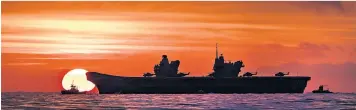  ??  ?? A glorious sight as HMS Queen Elizabeth is a silhouette in the rising sun. Right, two of the many supporters