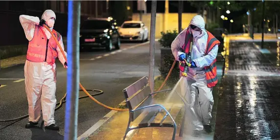  ?? CCLM ?? Dos operarios vestidos con equipos de protección individual desinfecta­n un banco público de Fuensalida (Toledo) por la noche