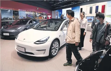  ?? AFP ?? People look at Tesla Model 3 cars at a showroom in Beijing on Wednesday.