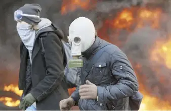  ??  ?? DOS MANIFESTAN­TES se protegen con máscaras durante los enfrentami­entos con la policia, tras reanudarse los disturbios en Kiev después de varias semanas de tregua.