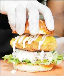  ??  ?? A handler tops a Krispy Fried Chk’n sandwich with a doughy pretzel bun
in Miami. (AP)