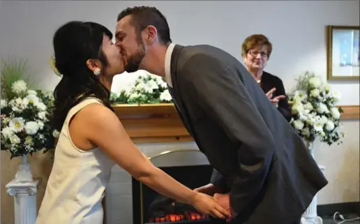  ?? PETER LEE, RECORD STAFF ?? Miku Yodoi and Eric Kipling kiss after getting married at the Wedding Belle Chapel at Kitchener City Hall on Tuesday. Officiant Pat Fretwell is in the background.
