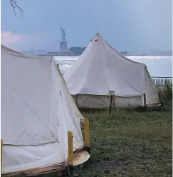  ?? ROBIN MARTIN/THE NEW MEXICAN ?? The Statue of Liberty is visible beyond the campsite’s canvas tents as a rain shower pelts the New Jersey shore in the background.