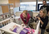  ?? CAROLYN VAN HOUTEN / WASHINGTON POST ?? Jason Davis and Samantha Mullen watch as Elizabeth Ottaway takes holiday-themed photos of their daughter, Phoebe Alan Davis, in the NICU at the Children’s National Medical Center in Washington.