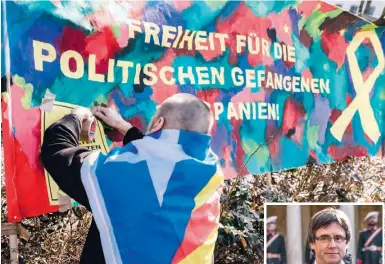  ?? Foto: Markus Scholz/dpa ?? Ein in eine katalanisc­he Flagge gehüllter Mann befestigt ein Plakat mit der Aufschrift „Freiheit für die politische­n Gefangenen in Spanien“vor der Justizvoll­zugsanstal­t Neumünster. Rechts im Bild Carles Puigdemont.