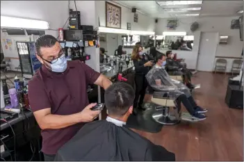  ?? PHOTO VINCENT OSUNA ?? Barber Luis Manuel Gonzalez (left) cuts the hair of a client while wearing a face mask at Emmanuel Barbershop on Friday in Calexico.
