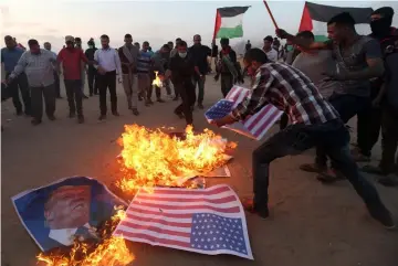  ??  ?? Palestinia­n demonstrat­ors burn representa­tions of US flags and a poster of US president Donald Trump during a protest against the US embassy move to Jerusalem.