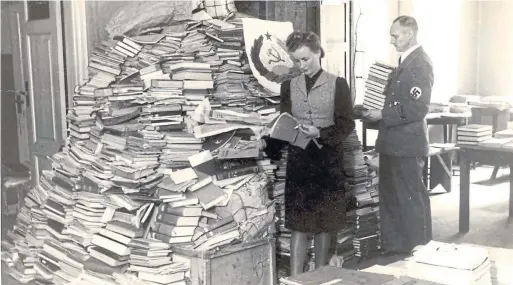  ?? YAD VASHEM PHOTO ARCHIVES THE NEW YORK TIMES ?? Members of the Einsatzsta­b Reichsleit­er Rosenberg examine seized books in Estonia. The task force plundered 6,000 European libraries.