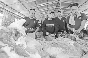  ??  ?? Ken (second left) helping some of the Bomba Petra Jaya staff cutting the meat before distributi­ng them as alms to the needy and to the staff of Bomba Petra Jaya and Immigratio­n Department Sarawak.