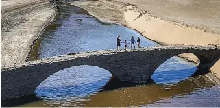  ??  ?? Secret bridge revealed... families cross the historic packhorse bridge uncovered in County Durham by drought, above and left. Right: How the reservoir normally looks