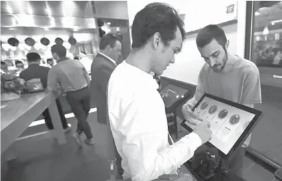  ?? Associated
Press ?? ABOVE: Charles Renwick, right, lead software engineer at Spyce Food Company, assists a customer with an order May 3 at the Spyce restaurant, which uses a robotic cooking process. Robots can’t yet bake a souffle or fold a burrito, but the new restaurant...