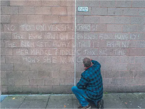  ??  ?? A man scrawls a message in chalk outside Dundee Job Centre in protest at Universal Credit.