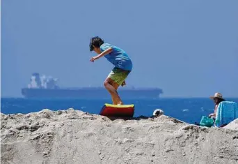  ?? Damian Dovarganes/Associated Press ?? A boy slides with a surf board on top of a sand berm in Seal Beach, Calif., on Friday. Officials in Southern California were also re-enforcing sand berms, built to protect low-lying coastal communitie­s against winter surf.